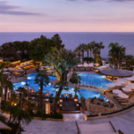 Πανοραμική θέα του Mediterranean Beach Hotel στη Λεμεσό με πισίνα και Μεσόγειο κατά το ηλιοβασίλεμα