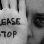 Γυναίκα υψώνει το χέρι της με το μήνυμα Please Stop, σε συμβολική εικόνα κατά της ενδοοικογενειακής βίας