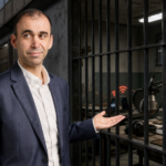 Πολιτική εικονογράφηση με τον βουλευτή του ΑΚΕΛ Ανδρέα Πασιουρτίδη μπροστά από κελιά, κινητά τηλέφωνα και εξοπλισμό podcast