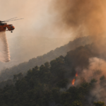 Πυροσβεστικό ελικόπτερο επιχειρεί πάνω από δασική πυρκαγιά σε συμβολική εικονογράφηση για τη σύγκρουση στην Ψάθα