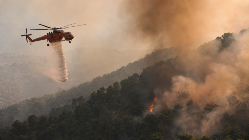 Πυροσβεστικό ελικόπτερο επιχειρεί πάνω από δασική πυρκαγιά σε συμβολική εικονογράφηση για τη σύγκρουση στην Ψάθα