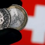 Νομίσματα ελβετικού φράγκου μπροστά από ελβετική σημαία