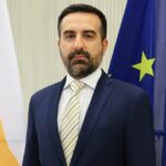 Ο υφυπουργός Μετανάστευσης Νικόλας Ιωαννίδης μπροστά στις σημαίες της Κύπρου και της Ευρωπαϊκής Ένωσης