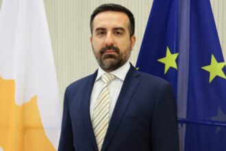Ο υφυπουργός Μετανάστευσης Νικόλας Ιωαννίδης μπροστά στις σημαίες της Κύπρου και της Ευρωπαϊκής Ένωσης