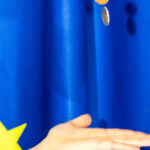 Χέρι και κέρματα ευρώ με φόντο την ευρωπαϊκή σημαία