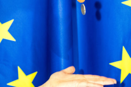 Χέρι και κέρματα ευρώ με φόντο την ευρωπαϊκή σημαία