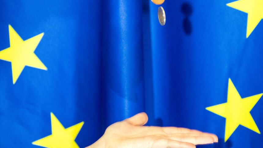 Χέρι και κέρματα ευρώ με φόντο την ευρωπαϊκή σημαία