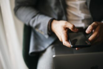 Άνδρας κρατά κινητό τηλέφωνο δίπλα σε φορητό υπολογιστή