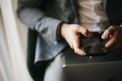 Άνδρας κρατά κινητό τηλέφωνο δίπλα σε φορητό υπολογιστή
